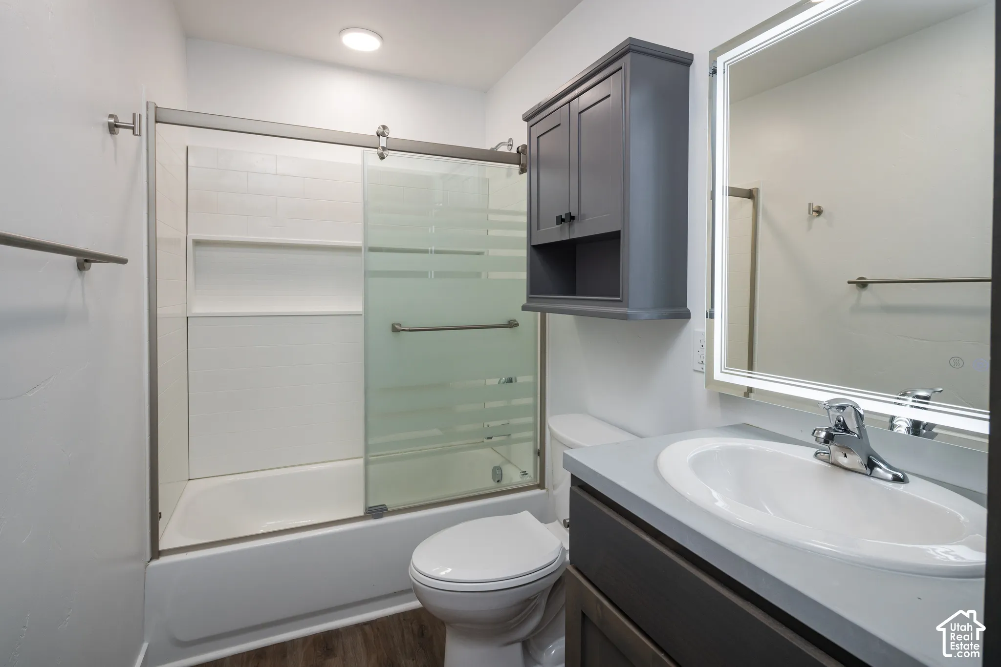 Bathtub with sliding glass shower doors, vanity with integrated sink, wall-mounted medicine cabinet, and wood-finish flooring