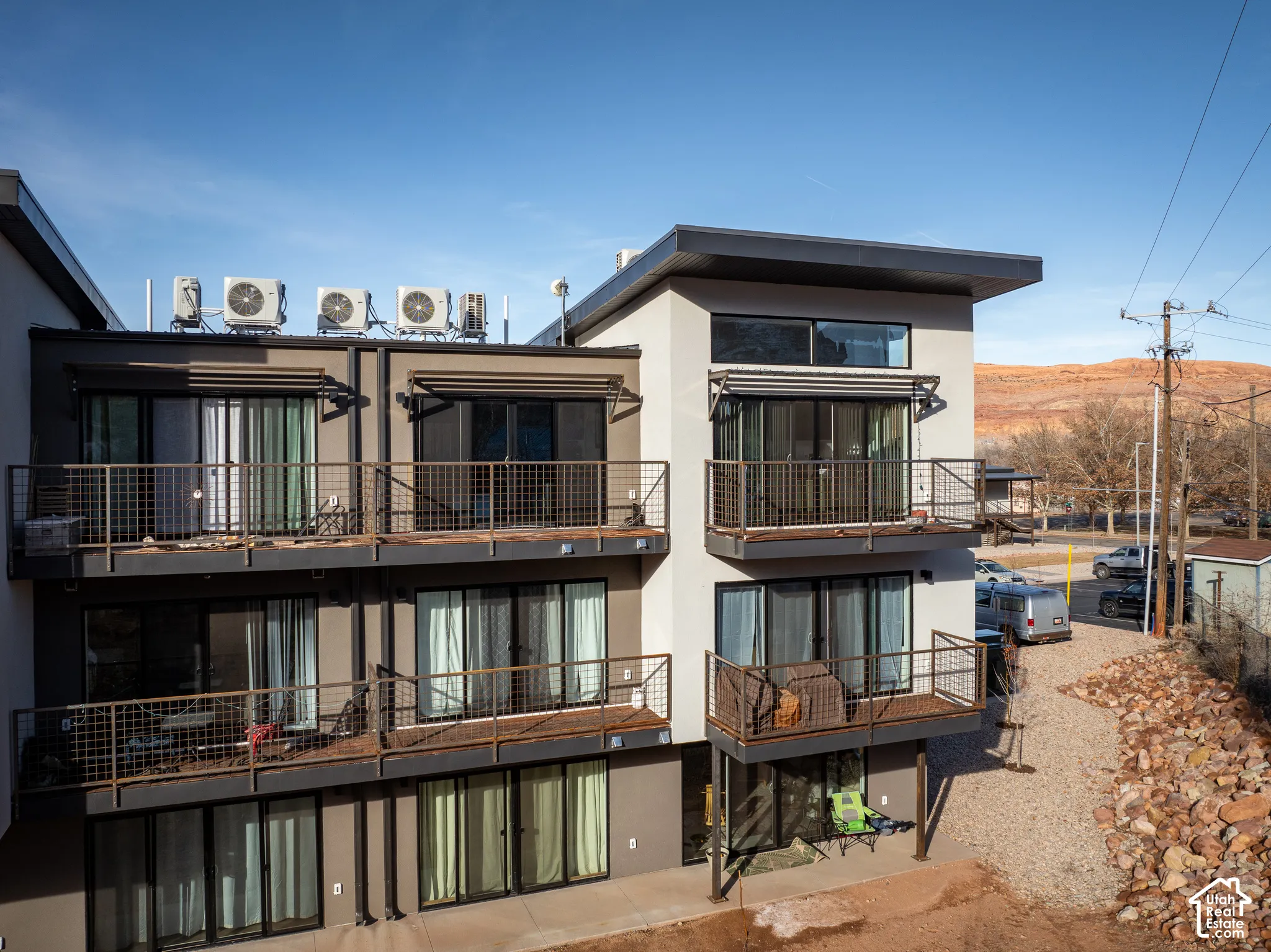 Modern multi-story building featuring multiple balconies with metal railings, sliding glass doors, and exterior awnings