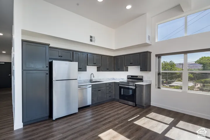 Kitchen featuring dark wood-finish cabinetry, stainless steel appliances, light-colored countertops, wood-finish flooring, and high ceilings with upper-level windows