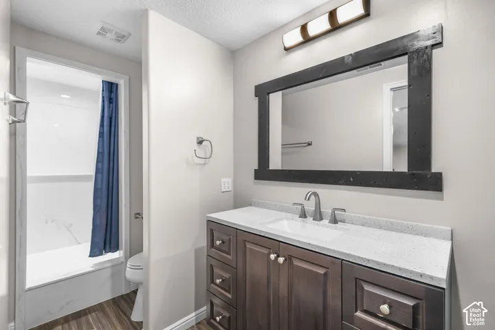Bathroom featuring a vanity with a white countertop, wood-finish flooring, a dark wood-framed mirror, and a shower with white surround