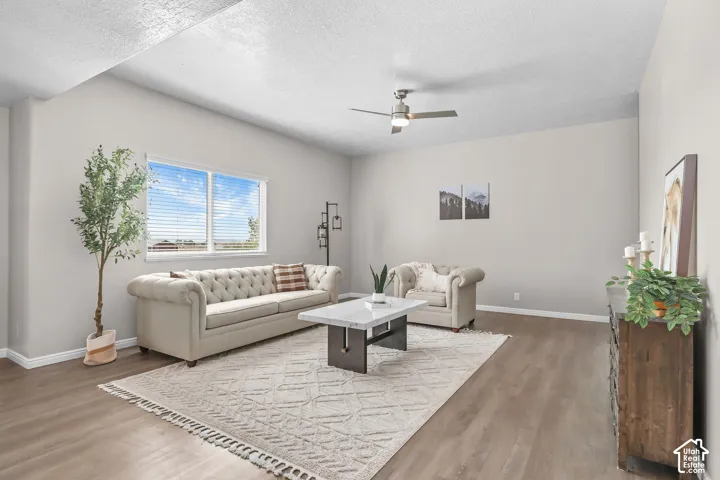 Vaulted ceiling with a ceiling fan, light gray wall paint, wood-finish flooring, and a large window with blinds