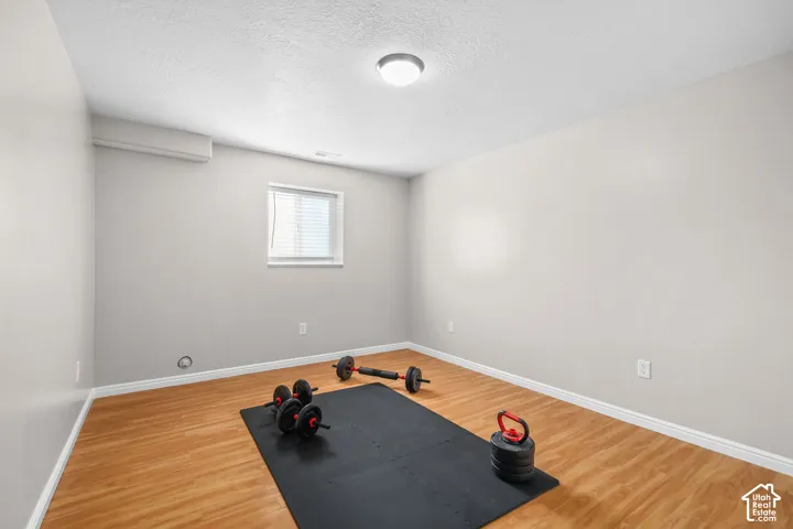 Hardwood-style flooring with a window featuring blinds, a ceiling-mounted light fixture, and a wall-mounted climate control unit