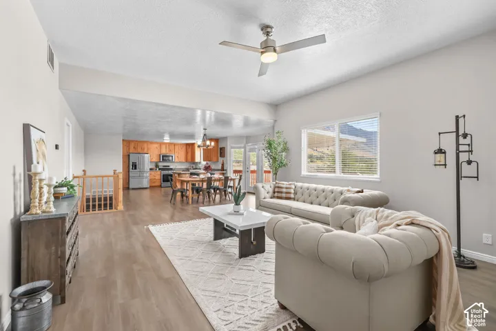 Open-concept living area featuring wood-finish flooring, a ceiling fan, and a large window with mountain scenery