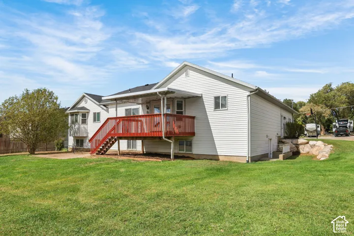 Expansive green lawn with a red stained deck, covered patio, and concrete patio