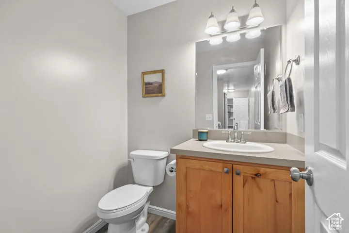 Wood-finish flooring, wood-finish vanity with square knobs, countertop with integrated sink, chrome faucet, and a three-light vanity fixture