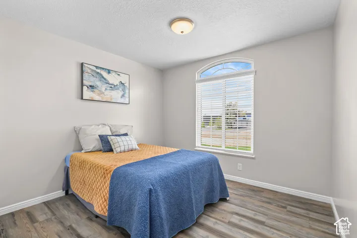 Wood-finish flooring, neutral wall paint, and an arched window with blinds