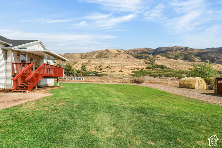 Expansive grassy area, wood-sided residence, red wood deck, covered porch, distant mountainous terrain