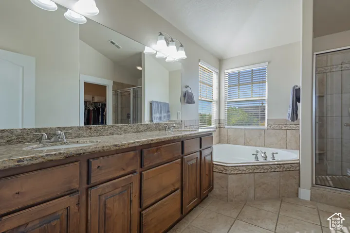 Dual vanity with undermount sinks and granite-style countertop, large framed mirror, corner soaking tub, tiled shower enclosure, and tiled flooring