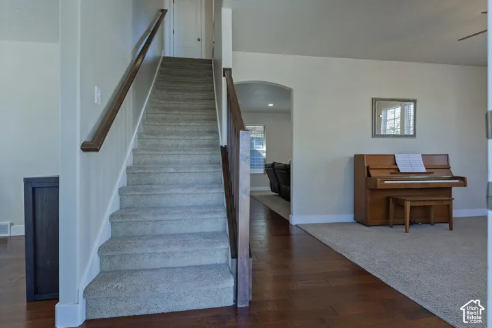Hardwood-style flooring, arched doorway, light-colored walls, carpeted stairs, and dark wood handrails