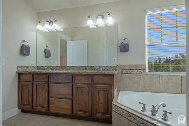 Dual vanity with a stone-finish countertop, wood-finish cabinetry, and an integrated corner bathtub with tiled surround