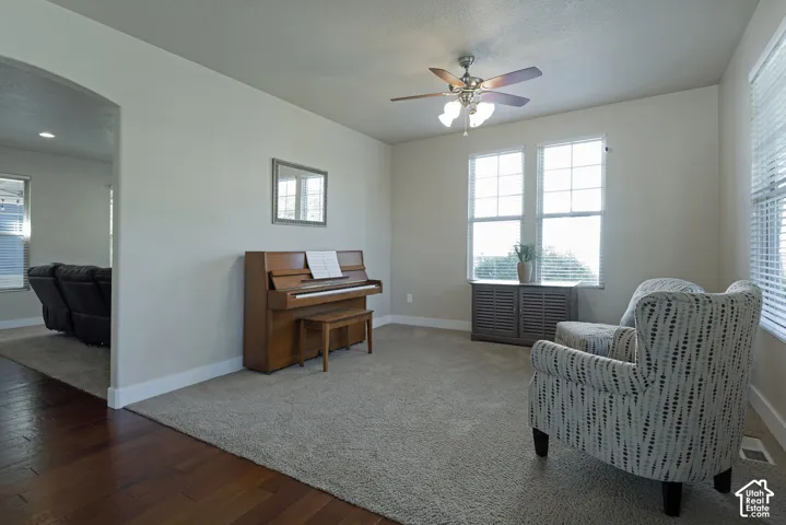 Carpeted room featuring a ceiling fan with integrated lighting, multiple windows with blinds, and an arched doorway