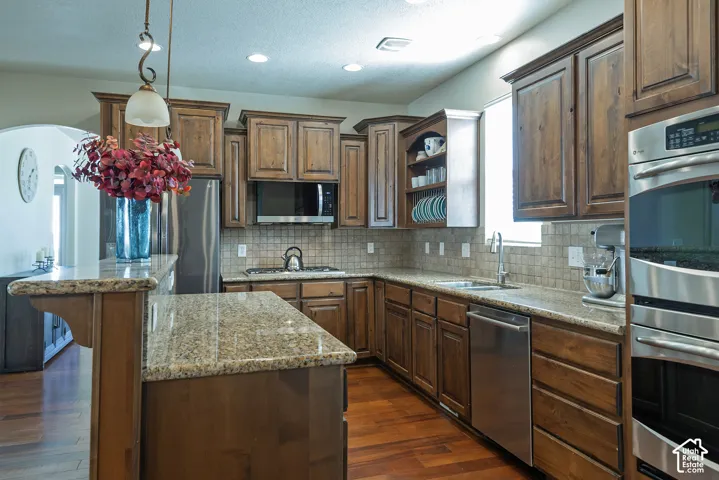 Kitchen featuring wood-finish flooring, granite countertops, wood cabinetry, stainless steel appliances, and a tiled backsplash