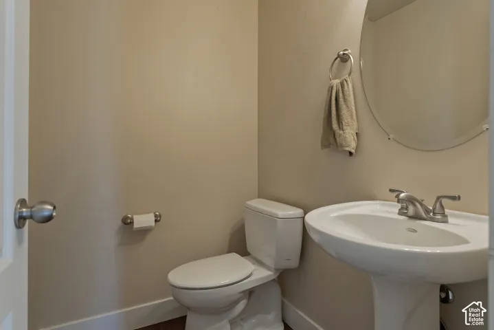 Pedestal sink with brushed nickel faucet, wall-mounted oval mirror, and a white toilet