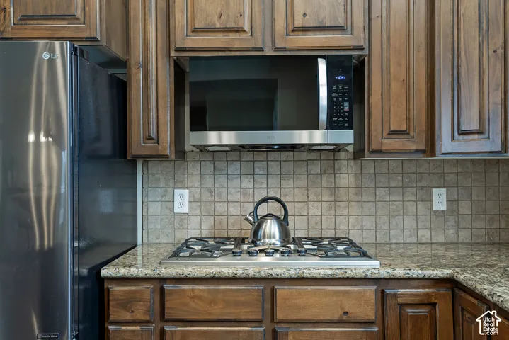 Built-in stainless steel microwave, gas cooktop, granite-style countertops, and full-height tiled backsplash