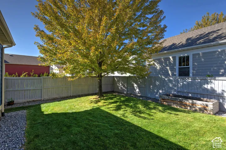 Private backyard featuring a manicured lawn, established tree, wood privacy fence, and a raised garden bed