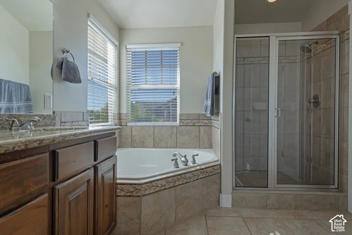 Built-in corner soaking tub, separate glass-enclosed shower, wood-finish vanity with countertop, and tile flooring
