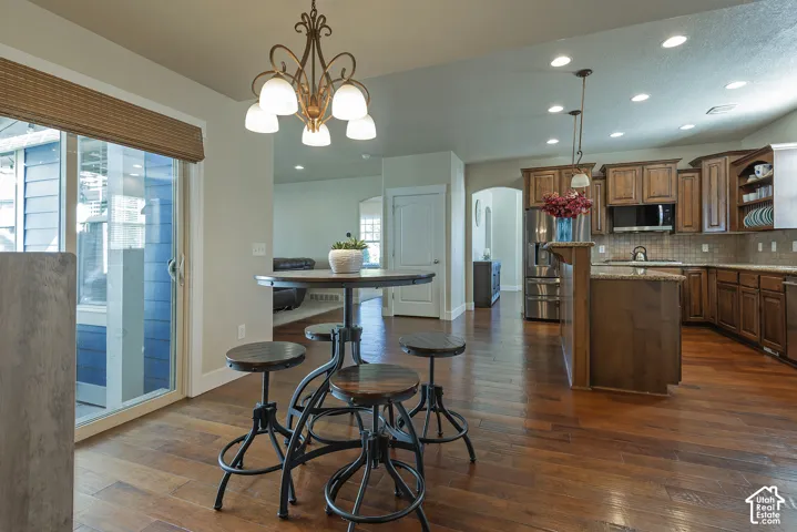Wood-finish flooring throughout, kitchen with wood cabinetry and stainless steel appliances, breakfast bar with pendant lighting, recessed lighting, and sliding glass door