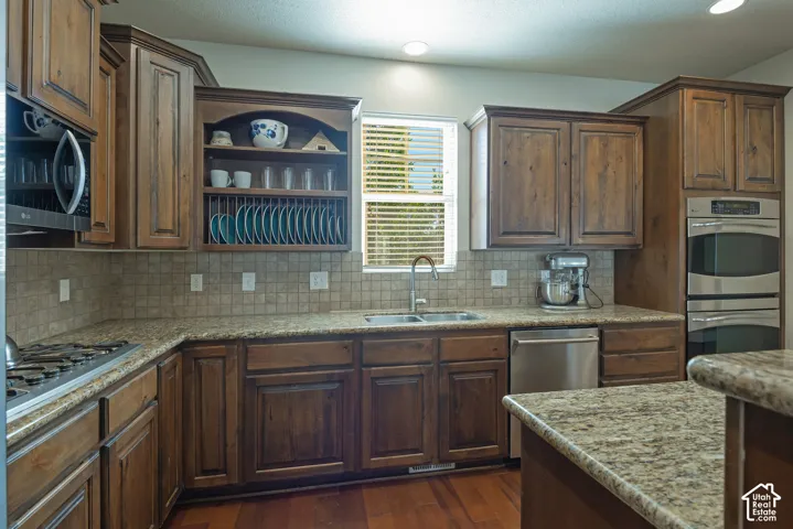Kitchen with rich wood cabinetry, stone countertops, a tile backsplash, and stainless steel appliances