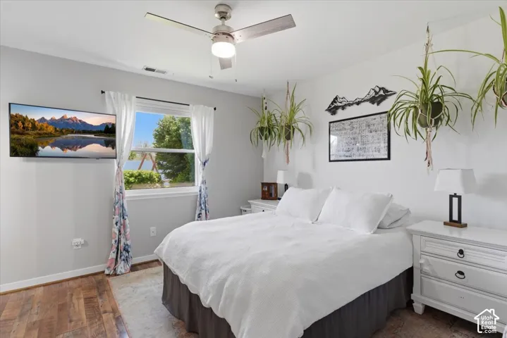 Wood-finish flooring, ceiling fan with light fixture, window with natural light, wall-mounted television, and neutral wall paint