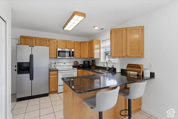Full kitchen featuring wood cabinetry, dark countertops, a stainless steel refrigerator, and white tile flooring