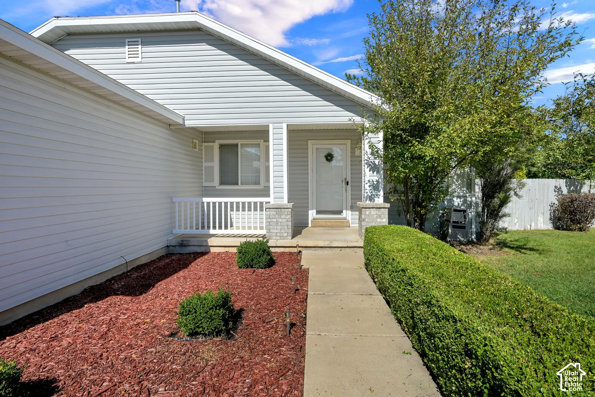 Light gray siding exterior with a covered front porch, white balustrade, and stone-clad columns
