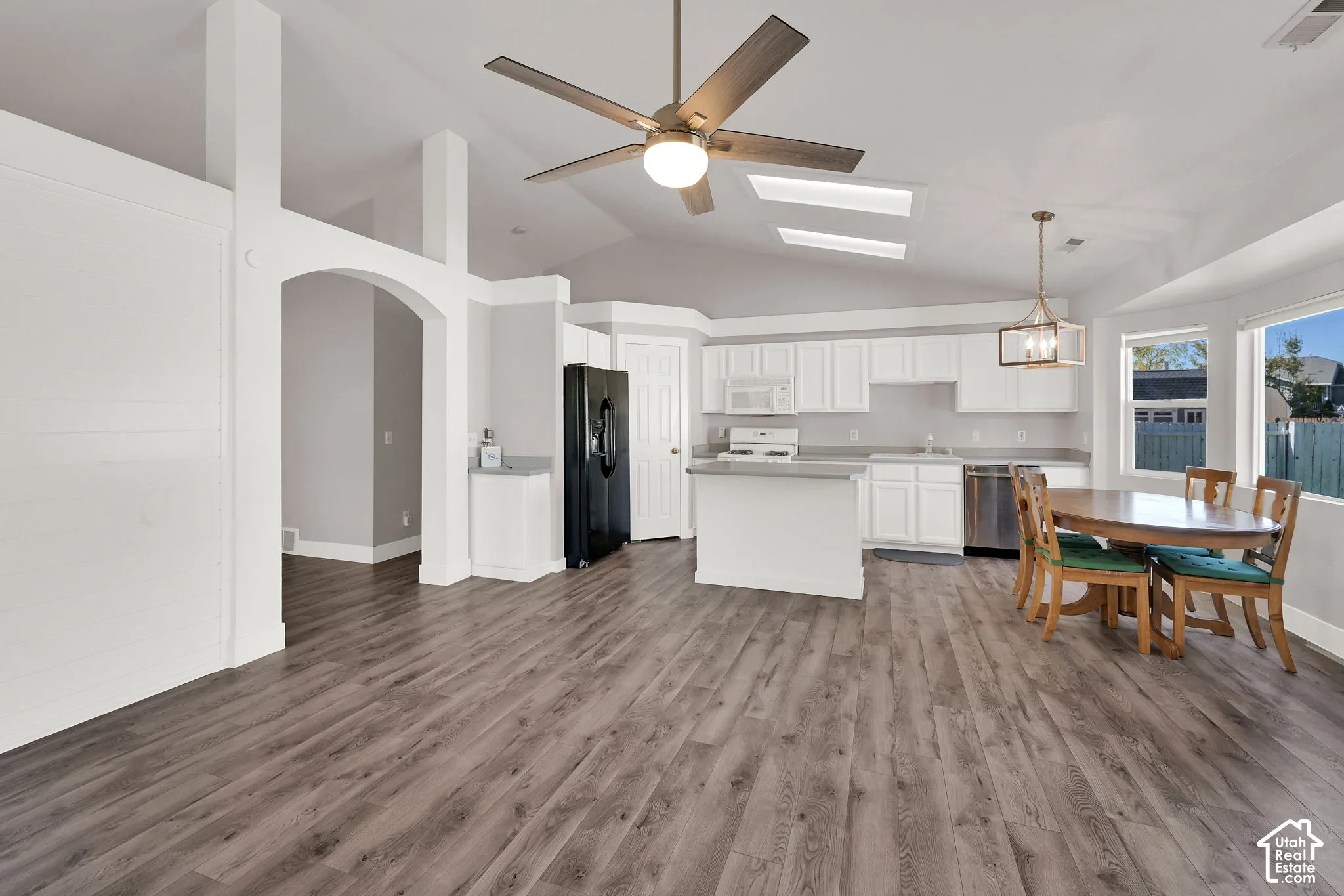 Vaulted ceilings, wood-finish flooring, white cabinetry, stainless steel appliances, and an arched entryway