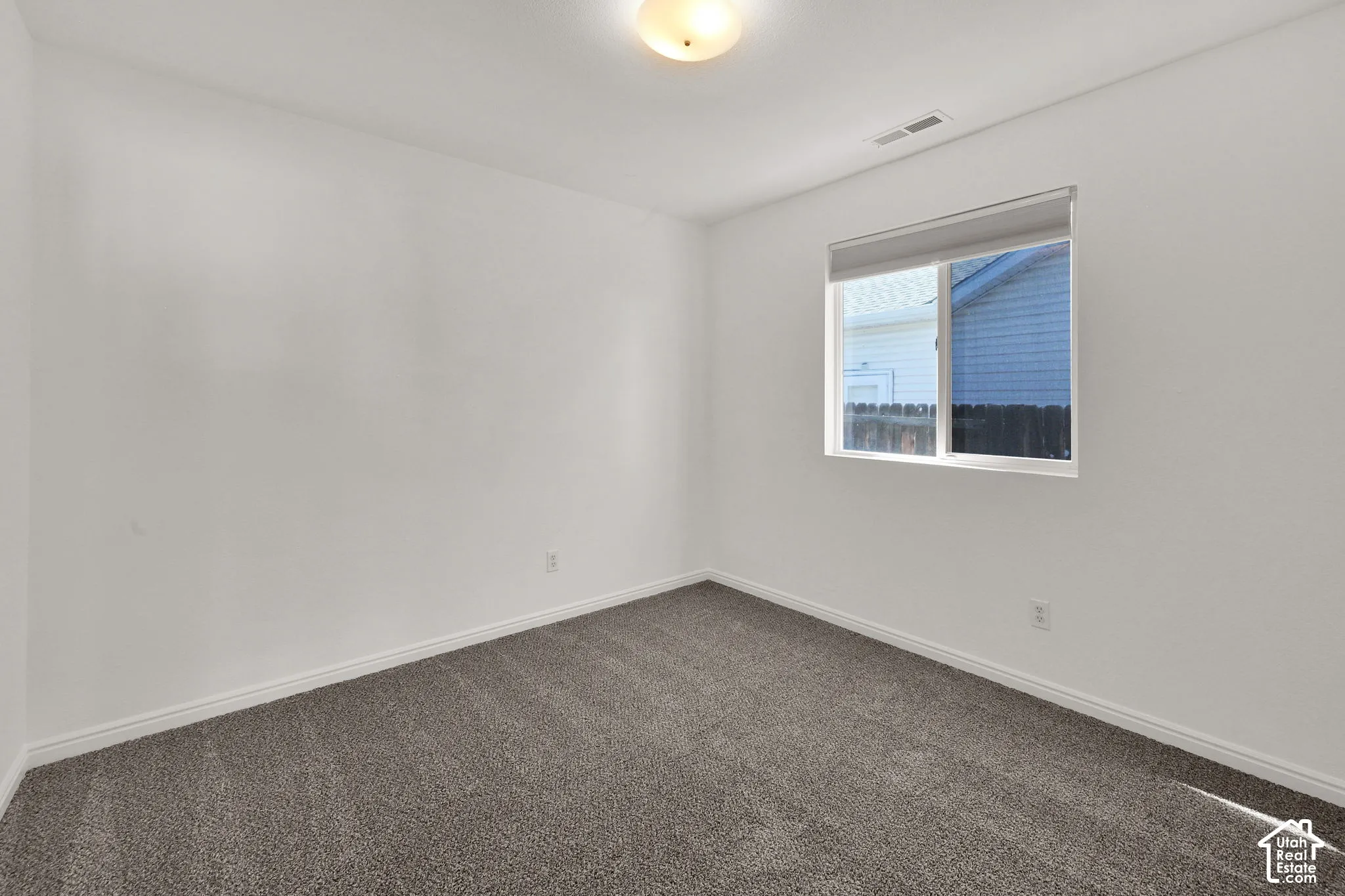 Neutral wall colors, plush carpeting, ceiling-mounted light fixture, and a window with shade
