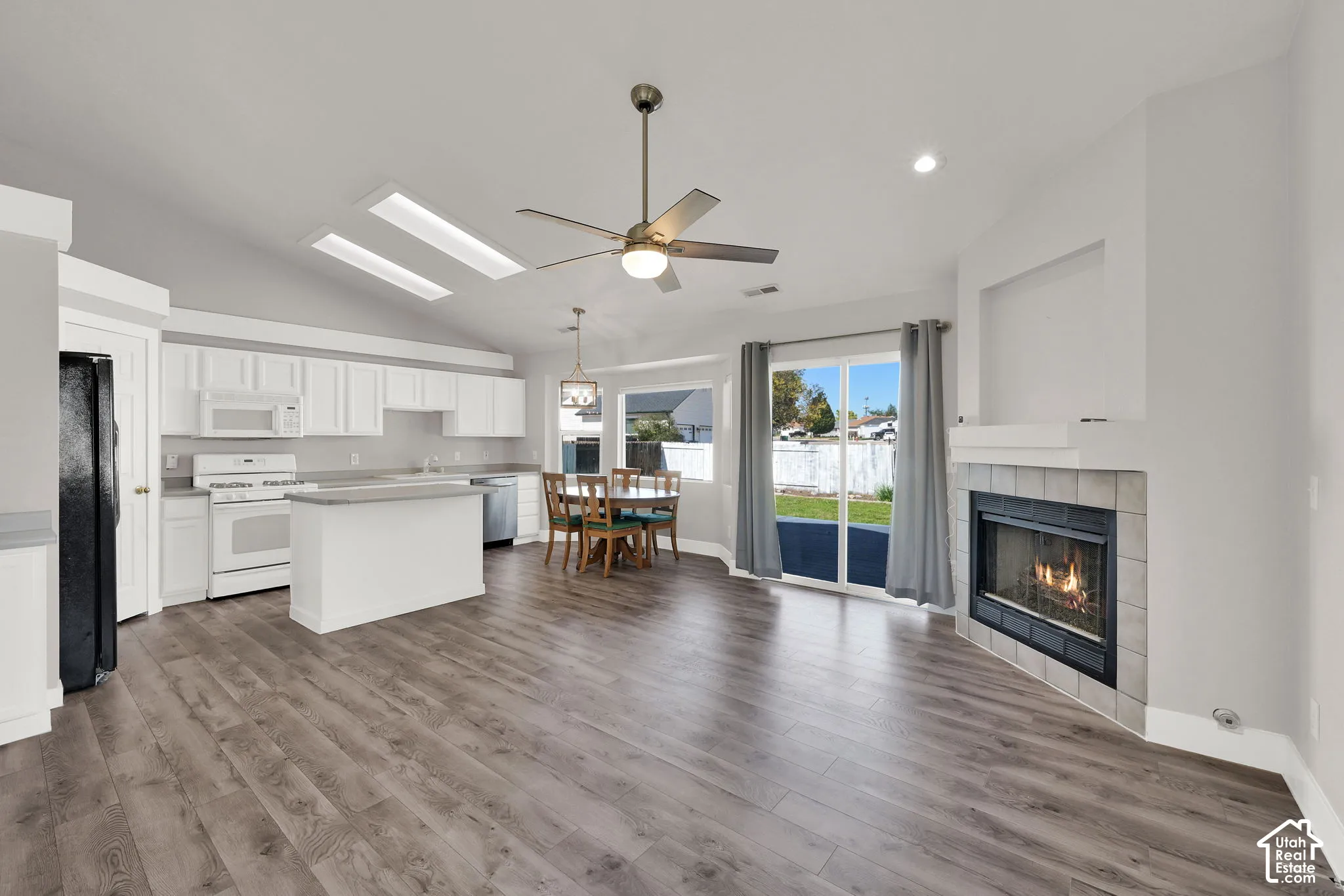 Vaulted ceilings, wood-finish flooring, white kitchen cabinetry, and a fireplace with tile surround