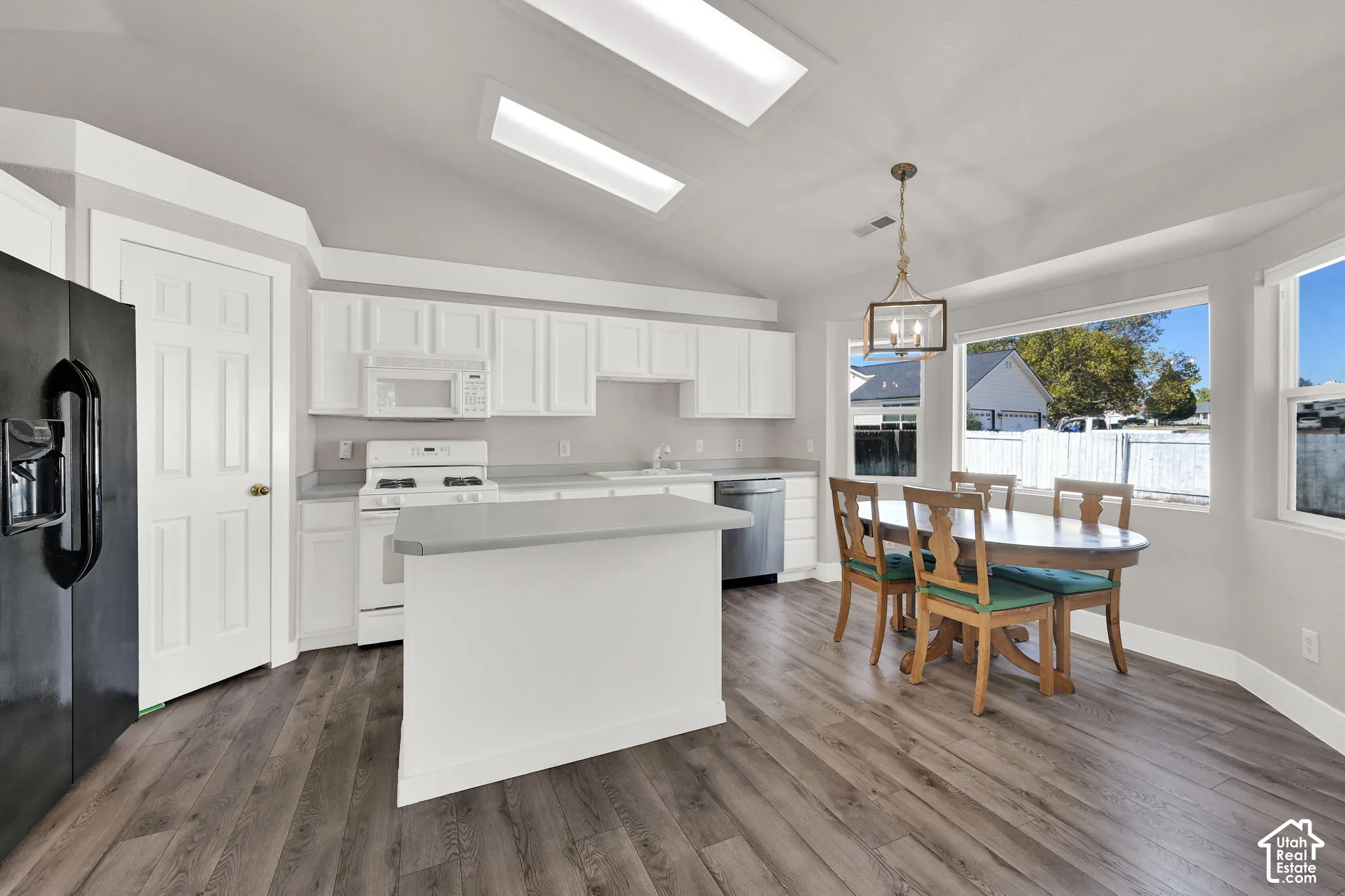 Vaulted ceiling, wood-finish flooring, white cabinetry, separate island, and large windows