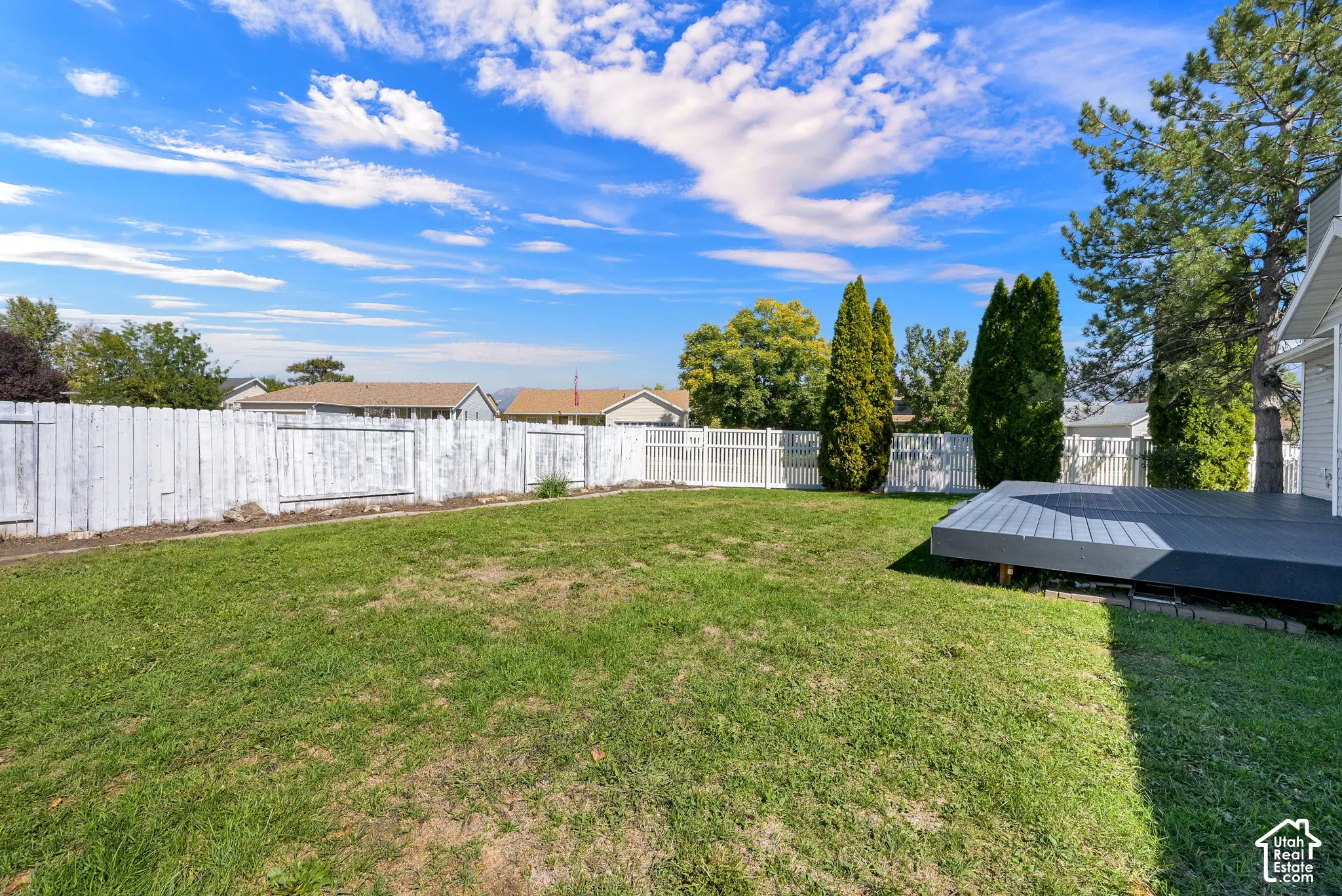 Expansive grassy yard with a composite deck, mature trees, and a full fence