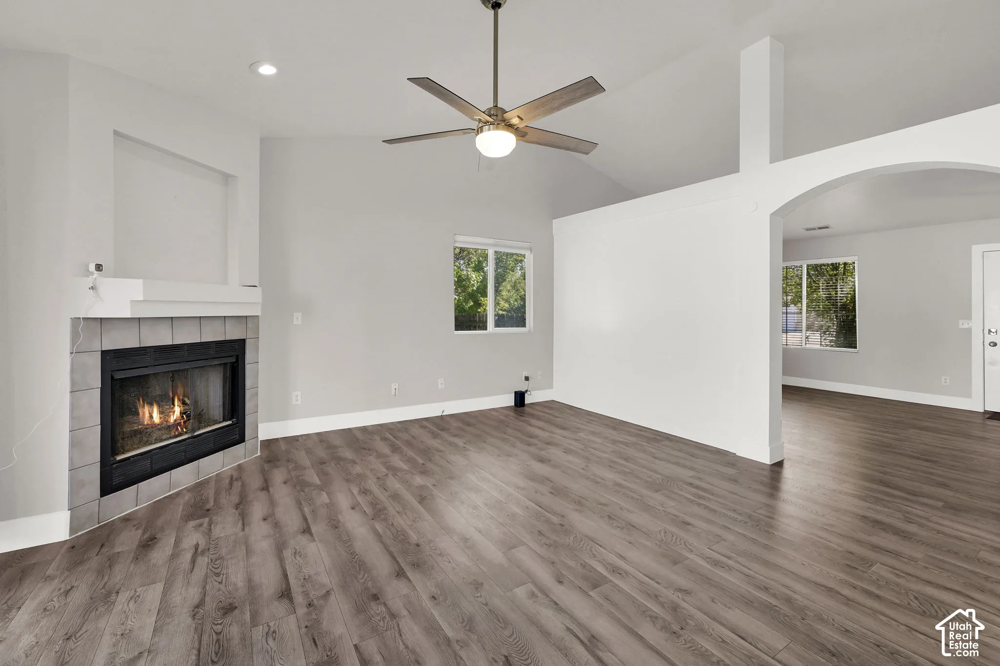Vaulted ceilings with a ceiling fan, wood-finish flooring, a fireplace with a tiled surround, and an arched entry