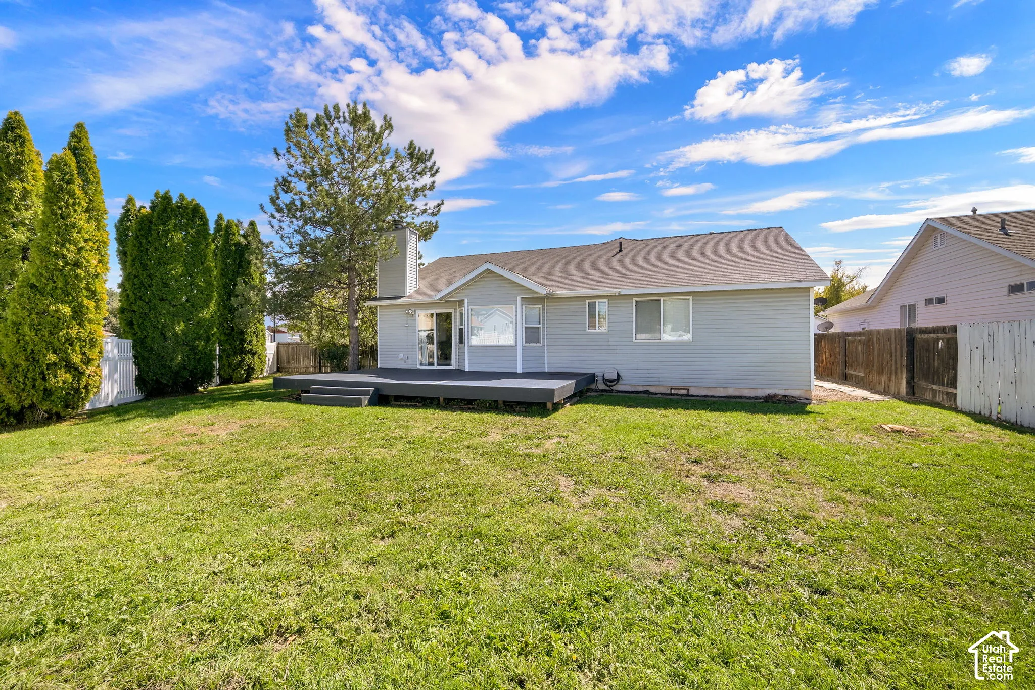 Spacious backyard featuring a substantial lawn, a large composite deck, and mature evergreen trees