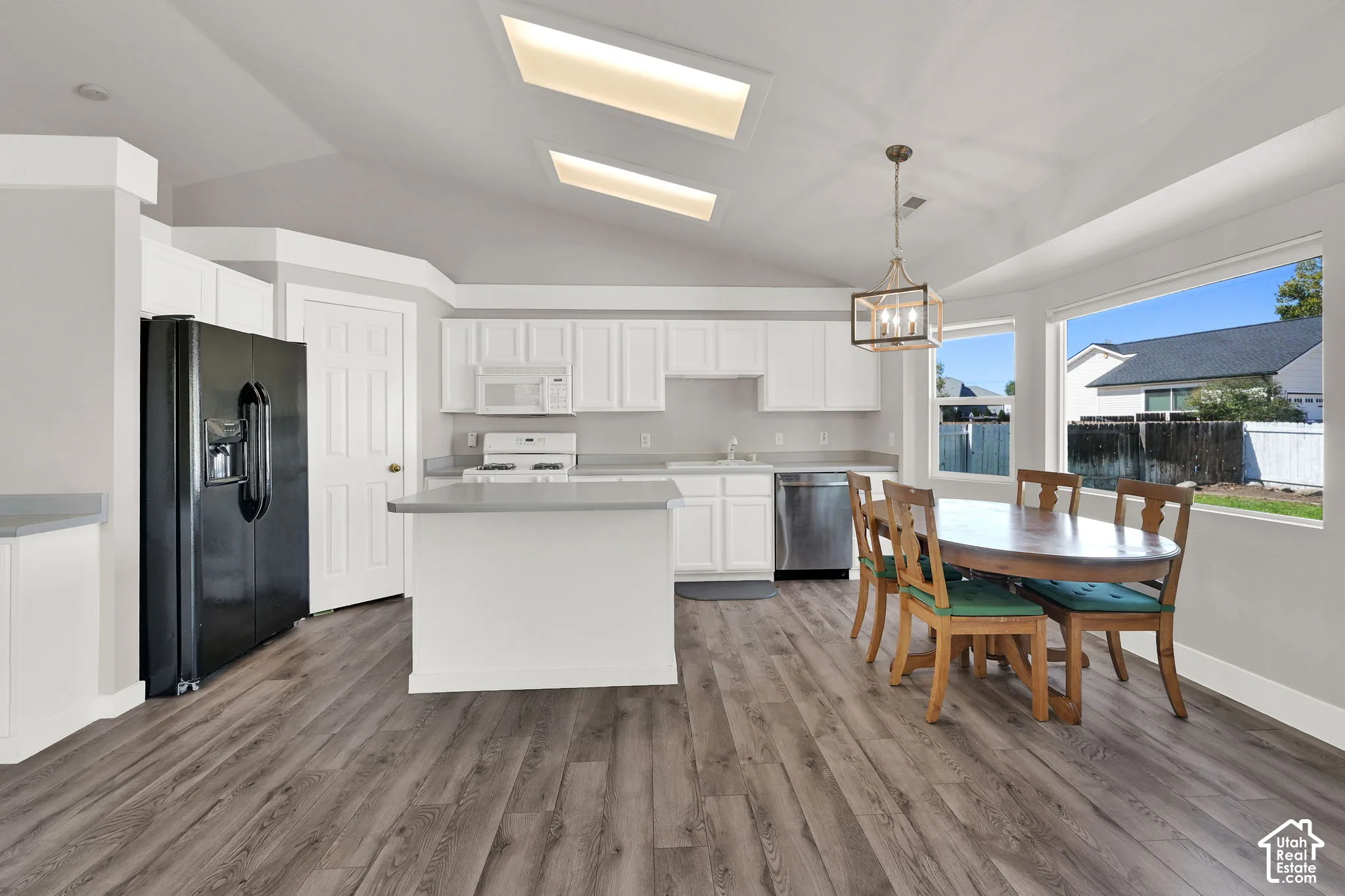 Vaulted ceiling, wood-finish flooring, white cabinetry, gray countertops, and large windows