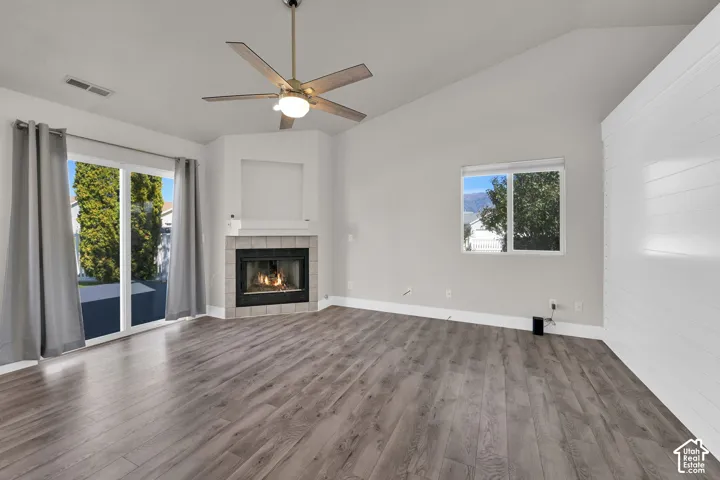 Vaulted ceiling with a ceiling fan, corner fireplace with tile surround, wood-finish flooring, sliding glass doors, and a window
