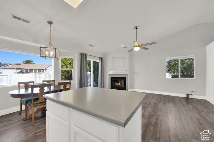 Kitchen island with solid surface countertop, vaulted ceilings, wood-finish flooring, and a fireplace with a mantel