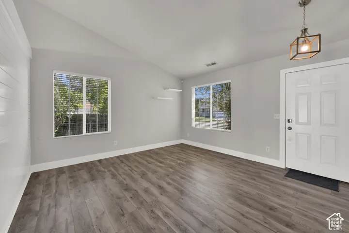 Vaulted ceiling, wood-finish flooring, two windows with blinds, panel door, and a geometric pendant light fixture