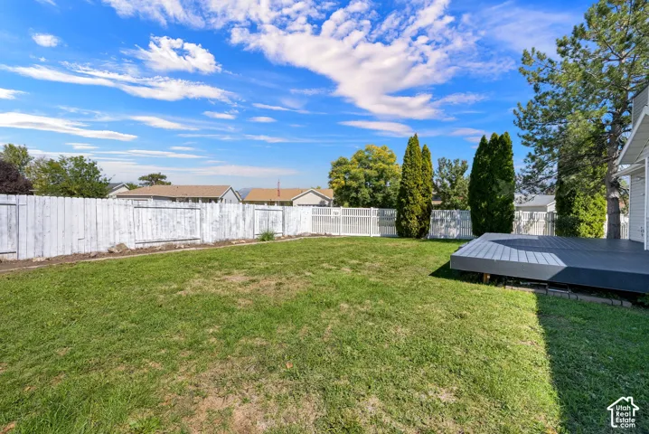 Expansive grassy yard with a composite deck, mature trees, and a full fence