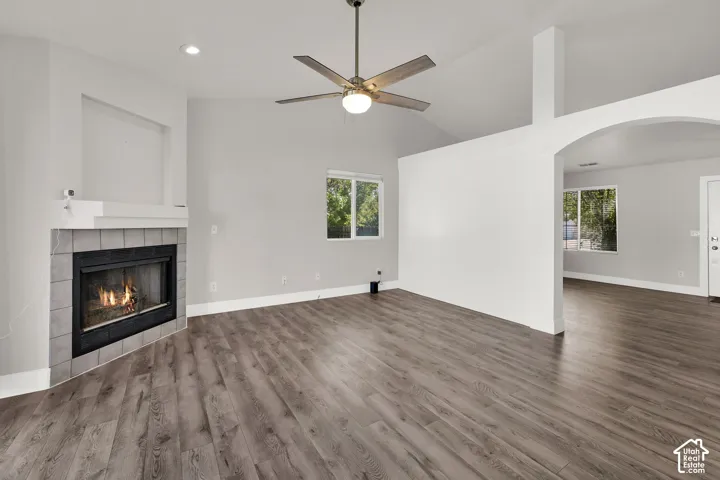 Vaulted ceilings with a ceiling fan, wood-finish flooring, a fireplace with a tiled surround, and an arched entry