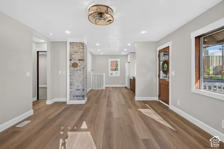 Wood-finish flooring, recessed lighting, exposed brick accent wall, white trim, and a wood-paneled door