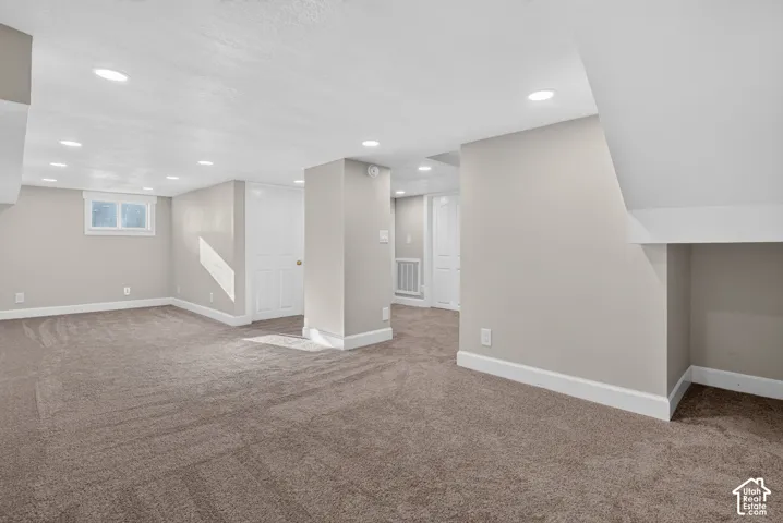 Expansive carpeted area with recessed lighting, neutral wall tones, and white trim