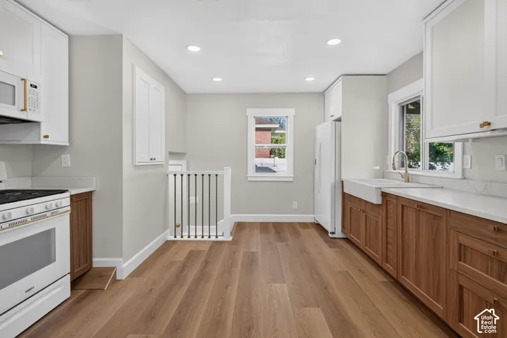 Kitchen featuring wood-finish flooring, white upper cabinetry, wood-finish lower cabinetry, a farmhouse sink, and recessed lighting