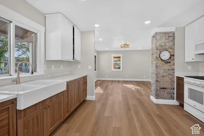 Kitchen with wood-finish flooring, white shaker upper cabinetry, wood-tone lower cabinetry, and a white apron-front sink with a brushed nickel faucet