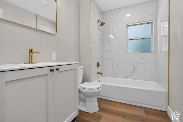 Modern vanity with integrated sink, gold-finish fixtures, white tile shower surround, and wood-finish flooring
