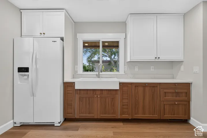 White shaker-style upper cabinetry, wood-finish lower cabinetry, farmhouse sink, white countertop, and wood-finish flooring