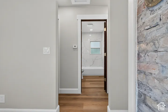 Exposed brick accent wall, wood-finish flooring, white wall paint, white trim, and a white interior door frame