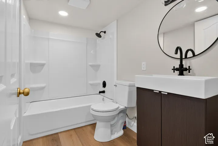 Tub-shower combination with matte black fixtures, wood-finish flooring, dark wood-finish vanity with white rectangular vessel sink, and a circular wall-mounted mirror