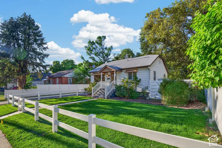 Single-story residence with a covered porch, white picket fence, mature trees, and a private side fence