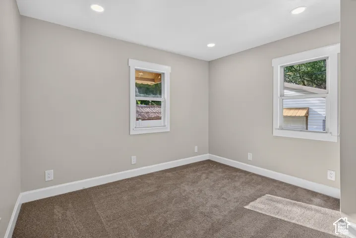 Recessed lighting, neutral wall paint, two windows, carpet flooring, and white trim
