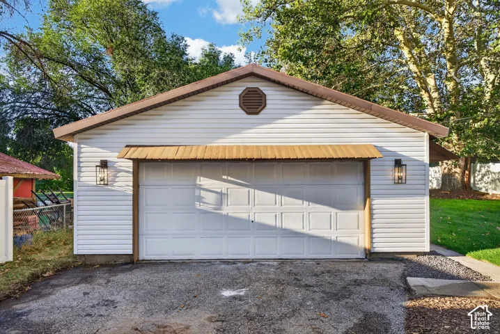 Detached garage featuring white vinyl siding, a brown shingle roof, decorative metal awning, and exterior wall sconces
