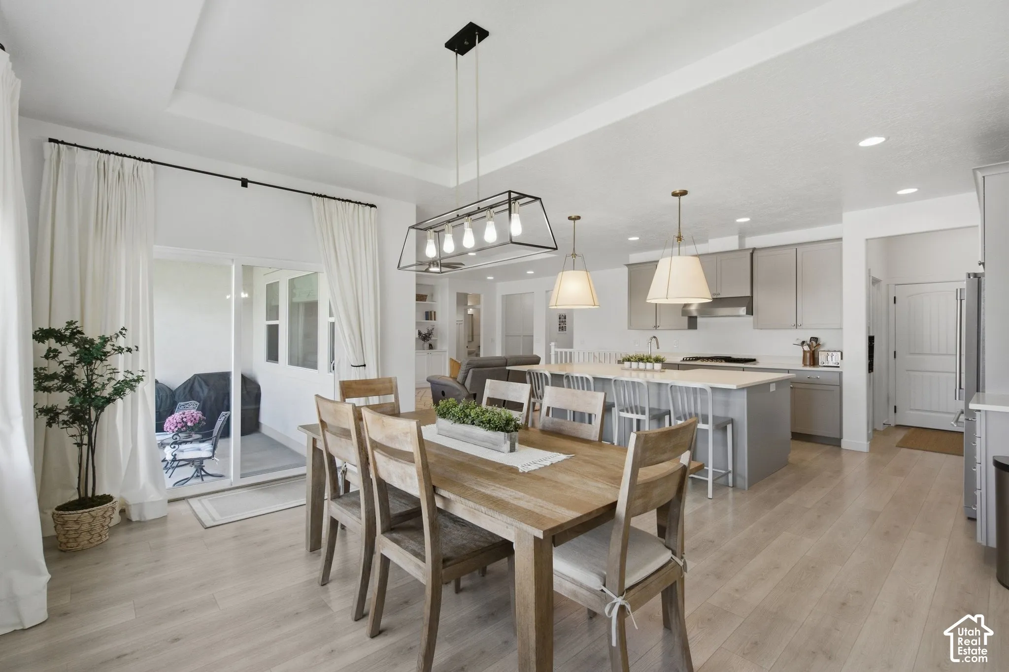 Tray ceiling with recessed lighting, light wood-finish flooring, white sliding glass doors, kitchen island with seating, and stainless steel appliances